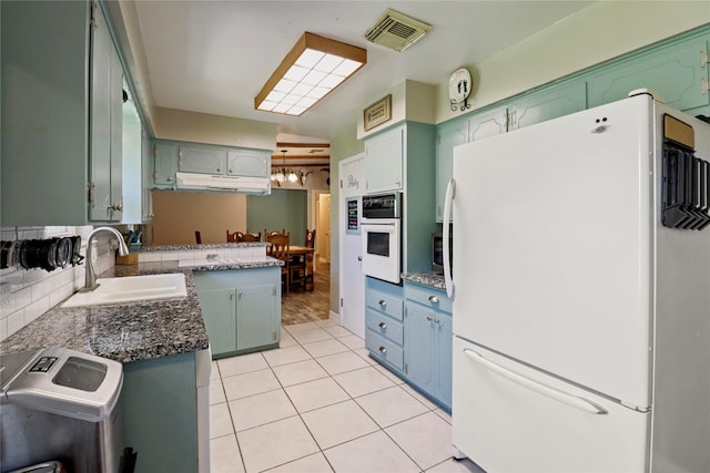 kitchen featuring white appliances, a sink, under cabinet range hood, light tile patterned flooring, and green cabinetry
