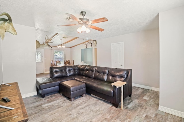 living area featuring a textured ceiling, ceiling fan, wood finished floors, baseboards, and lofted ceiling