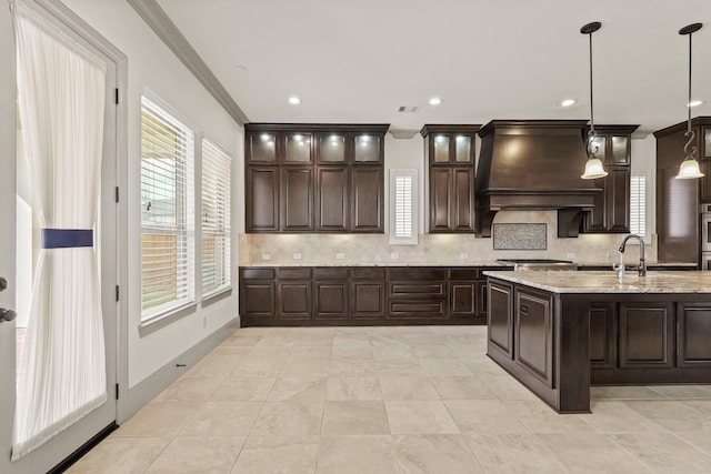67 Quiet Vista Dr, Sugar Land, TX 77498 - kitchen featuring custom range hood, backsplash, dark brown cabinets, crown molding, and decorative light fixtures