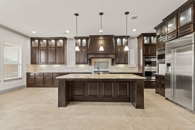 67 Quiet Vista Dr, Sugar Land, TX 77498 - kitchen featuring stainless steel appliances, custom exhaust hood, dark brown cabinetry, backsplash, and a center island with sink