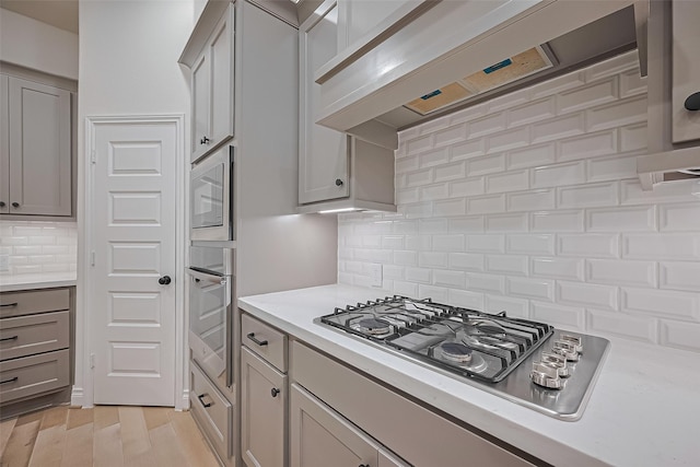 kitchen featuring stainless steel appliances, gray cabinets, tasteful backsplash, and light countertops