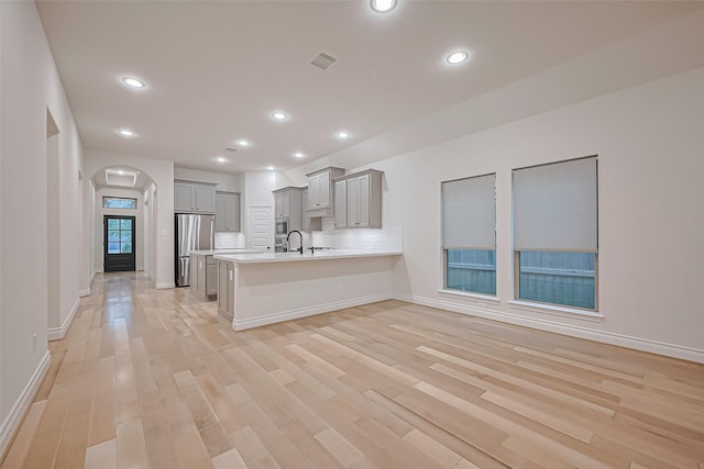 kitchen featuring freestanding refrigerator, gray cabinets, arched walkways, a peninsula, and light countertops