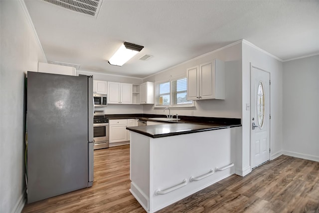 5311 Perry Ave, Galveston, TX 77551 - kitchen featuring appliances with stainless steel finishes, a sink, dark countertops, crown molding, and a peninsula