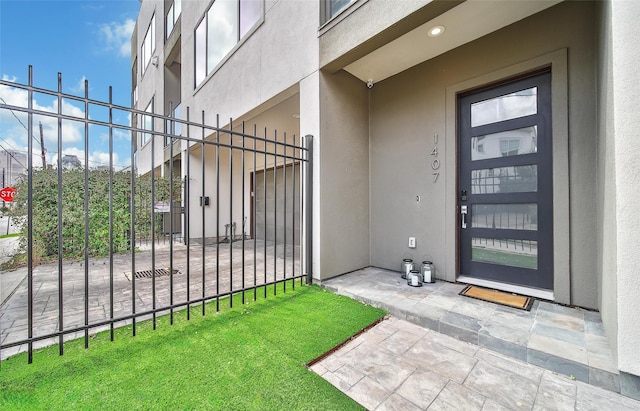 view of exterior entry featuring stucco siding and fence