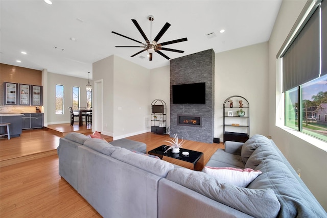 living area featuring light wood finished floors, a stone fireplace, ceiling fan, and recessed lighting