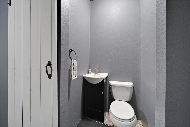bathroom with vanity, toilet, and a textured wall