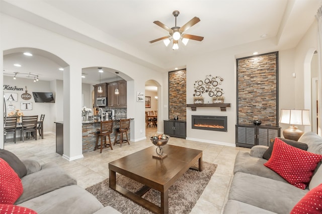19315 S Cottonwood Green Ln, Cypress, TX 77433 - living room featuring a ceiling fan, arched walkways, a tray ceiling, light tile patterned floors, and a glass covered fireplace