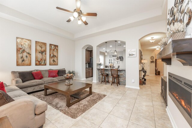 19315 S Cottonwood Green Ln, Cypress, TX 77433 - living area featuring arched walkways, ceiling fan, a raised ceiling, light tile patterned floors, and a glass covered fireplace