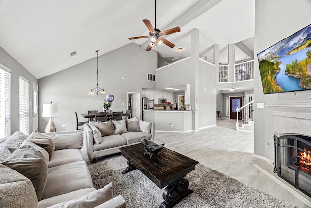 living room featuring high vaulted ceiling, light wood-style flooring, ceiling fan, a chandelier, and a high end fireplace