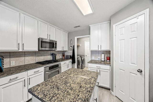 kitchen with stainless steel appliances, washing machine and clothes dryer, white cabinets, a center island, and dark stone countertops
