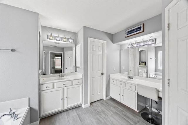 bathroom with two vanities, wood finished floors, baseboards, and a bath