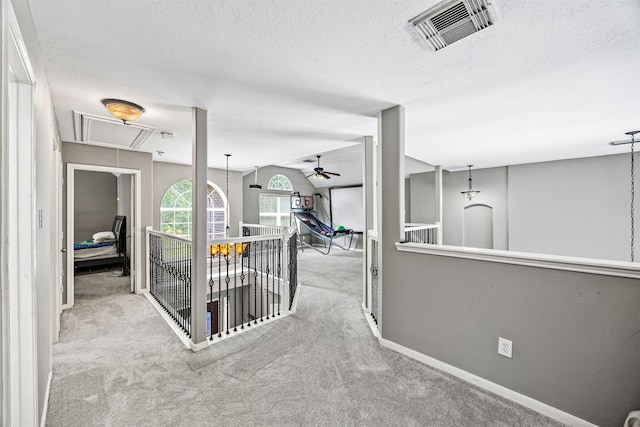 hallway featuring attic access, carpet, a textured ceiling, baseboards, and an upstairs landing