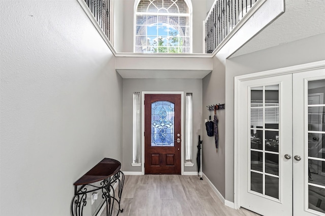 foyer with french doors, wood finished floors, baseboards, and a towering ceiling
