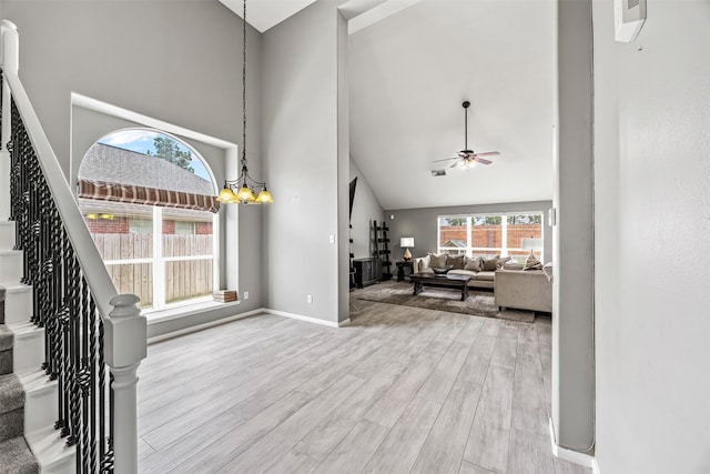 living room featuring high vaulted ceiling, a ceiling fan, wood finished floors, stairs, and baseboards