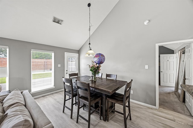 dining area featuring light wood-style flooring, baseboards, and high vaulted ceiling
