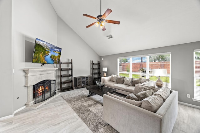 living area with ceiling fan, a premium fireplace, high vaulted ceiling, light wood-style floors, and baseboards