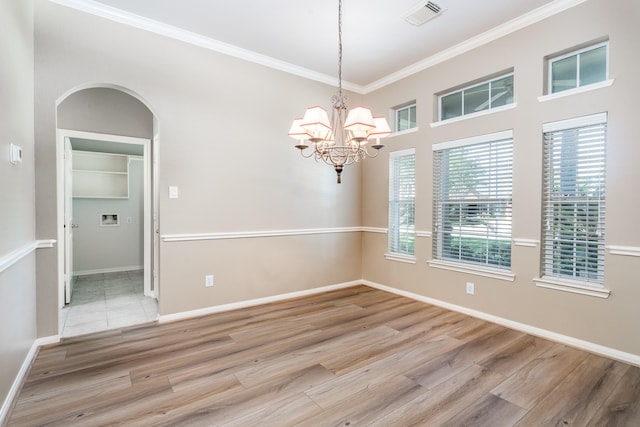 spare room with wood finished floors, a chandelier, ornamental molding, and arched walkways