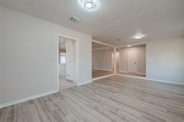 empty room with light wood finished floors, baseboards, and a textured ceiling