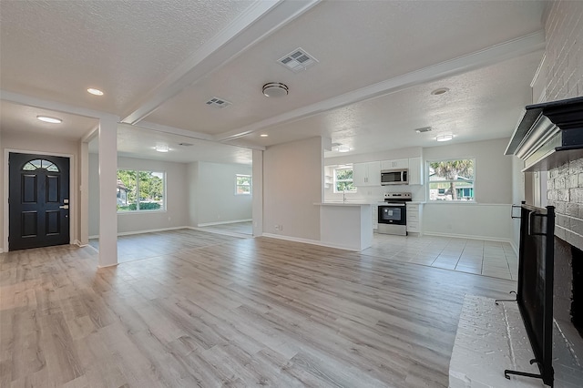 unfurnished living room with a textured ceiling, baseboards, healthy amount of natural light, a fireplace, and light wood-style floors
