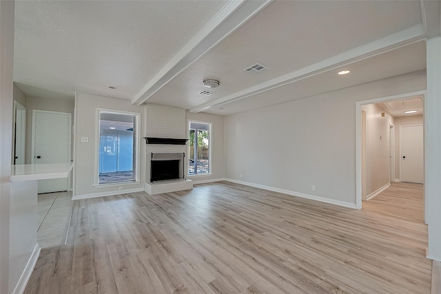 unfurnished living room with light wood finished floors, baseboards, beamed ceiling, a fireplace, and a textured ceiling