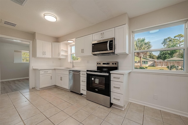 kitchen with appliances with stainless steel finishes, open shelves, light countertops, and white cabinetry
