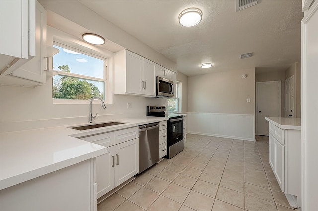 kitchen with appliances with stainless steel finishes, a sink, white cabinetry, light countertops, and a textured ceiling