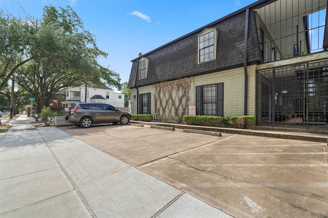 3402 Garrott St Unit 13, Houston, TX 77006 - view of home's exterior with brick siding, mansard roof, uncovered parking, and a shingled roof