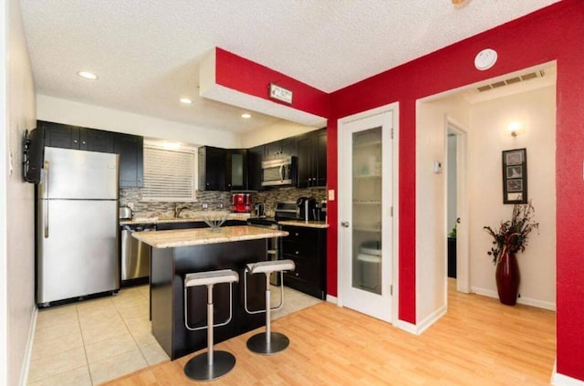 16631 Henry Morgan Rd, Jamaica Beach, TX 77554 - kitchen featuring stainless steel appliances, dark cabinetry, tasteful backsplash, a center island, and a breakfast bar area