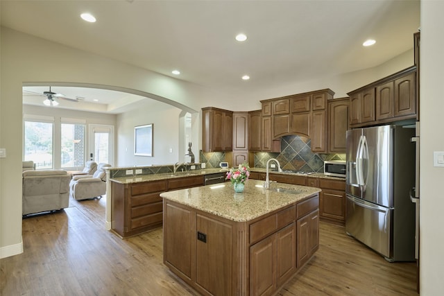 13606 Oak Harbor Bnd, Cypress, TX 77429 - kitchen with stainless steel appliances, arched walkways, a ceiling fan, a kitchen island with sink, and light wood finished floors