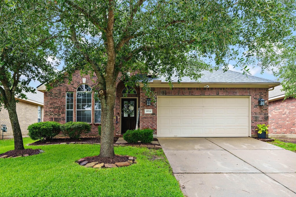 8934 Headstall Dr, Tomball, TX 77375 - view of front of house featuring concrete driveway, brick siding, a garage, and a front lawn