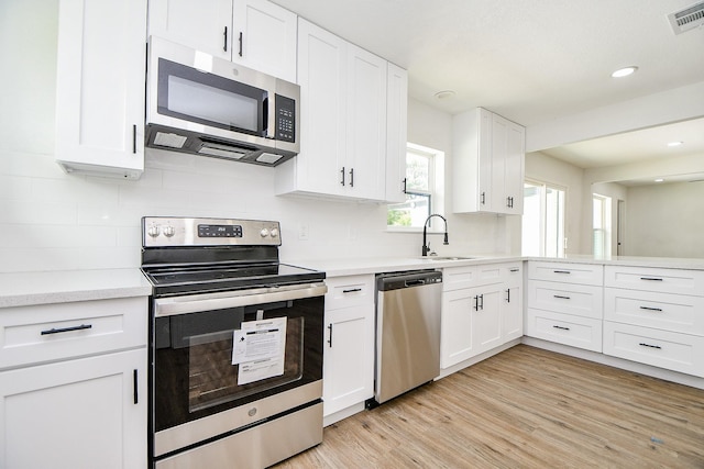 1915 Springrock Ln, Houston, TX 77080 - kitchen featuring appliances with stainless steel finishes, a sink, light wood-type flooring, white cabinetry, and backsplash