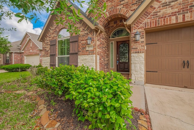 view of exterior entry with brick siding, an attached garage, driveway, and stone siding
