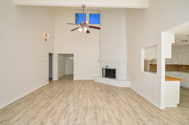 unfurnished living room with ceiling fan, a high ceiling, a fireplace, light wood-style flooring, and baseboards