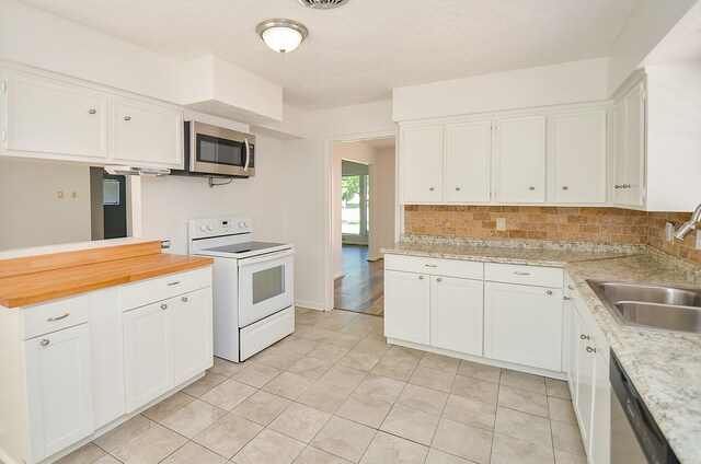 kitchen with stainless steel appliances, a sink, light tile patterned flooring, and white cabinetry