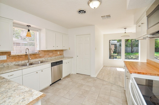 kitchen with a sink, stainless steel appliances, backsplash, white cabinets, and light tile patterned floors