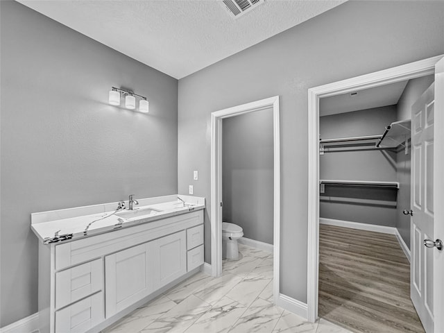 full bath featuring marble finish flooring, toilet, a walk in closet, baseboards, and a textured ceiling