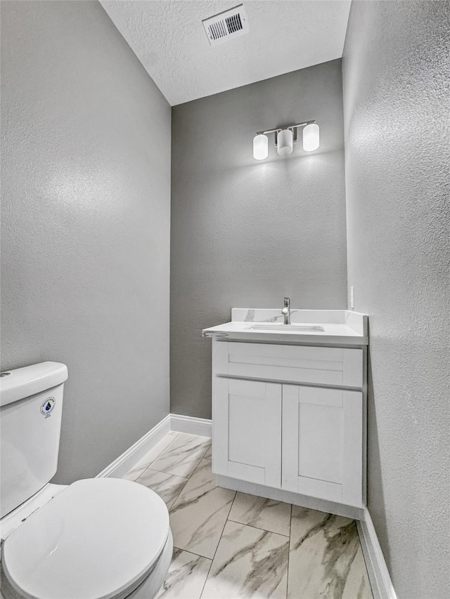 bathroom featuring baseboards, marble finish flooring, vanity, toilet, and a textured wall
