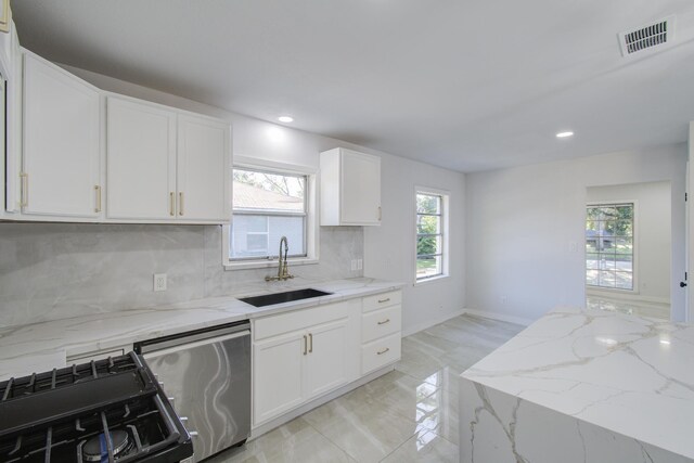 kitchen featuring a sink, stainless steel dishwasher, gas range oven, tasteful backsplash, and light stone countertops