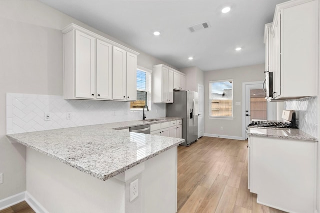 kitchen featuring baseboards, a peninsula, white cabinets, a sink, and recessed lighting