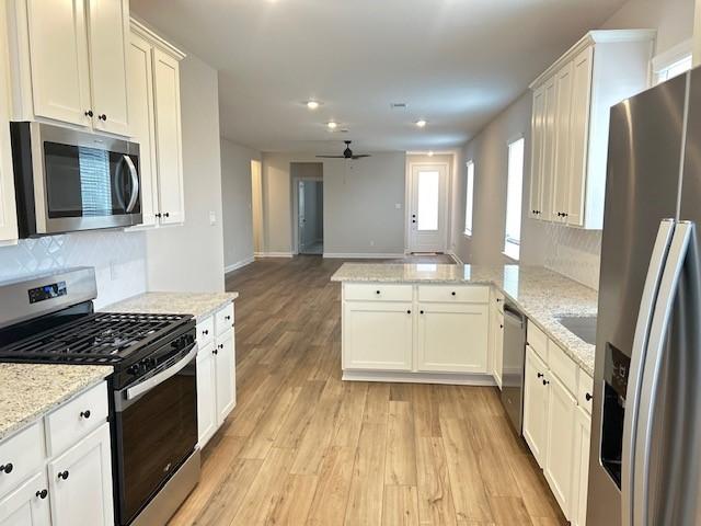 kitchen with appliances with stainless steel finishes, a peninsula, open floor plan, light wood-style floors, and decorative backsplash
