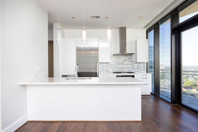 kitchen featuring a sink, wall chimney exhaust hood, stainless steel built in fridge, modern cabinets, and white cabinetry