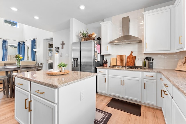21811 Gibson Desert Dr, Cypress, TX 77433 - kitchen with wall chimney range hood, appliances with stainless steel finishes, light wood finished floors, a kitchen island, and white cabinetry