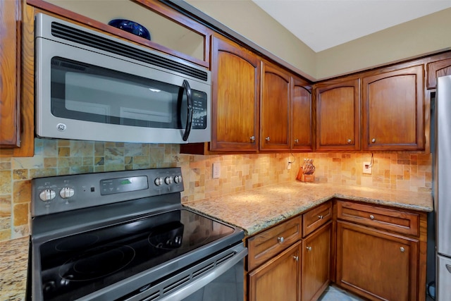 2810 Cottonwood Dr, Katy, TX 77493 - kitchen with range with electric cooktop, stainless steel microwave, backsplash, light stone countertops, and brown cabinetry