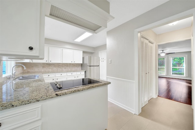 kitchen with a sink, freestanding refrigerator, black electric cooktop, plenty of natural light, and a wainscoted wall