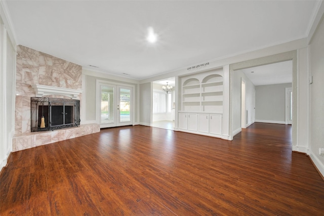 unfurnished living room with wood finished floors, a chandelier, built in features, a large fireplace, and crown molding
