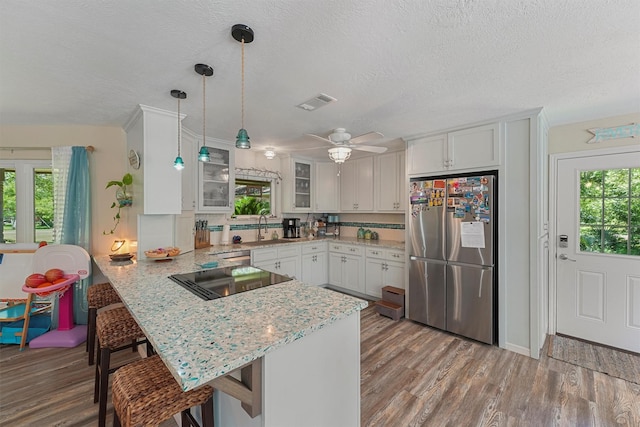 4701 County Road 747a, Brazoria, TX 77422 - kitchen featuring stainless steel refrigerator, a peninsula, black electric cooktop, wood finished floors, and glass insert cabinets
