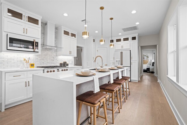1118 W Cottage St, Houston, TX 77009 - kitchen with wall chimney exhaust hood, white appliances, tasteful backsplash, a kitchen island with sink, and light wood finished floors