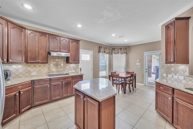 24628 Hosford Meadows Dr, Porter, TX 77365 - kitchen featuring stainless steel gas stovetop, under cabinet range hood, backsplash, a kitchen island, and light stone countertops