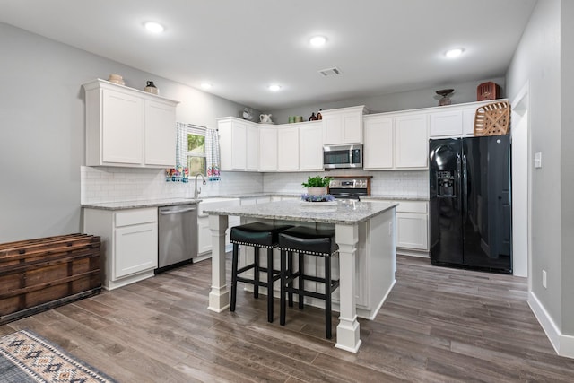 8729 Nathan Dr, Waller, TX 77484 - kitchen with stainless steel appliances, white cabinetry, a kitchen island, decorative backsplash, and dark wood-style floors