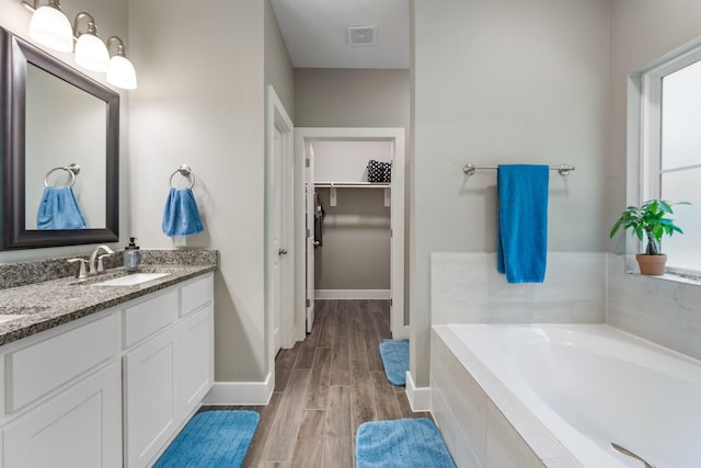 8729 Nathan Dr, Waller, TX 77484 - bathroom featuring a spacious closet, wood finished floors, double vanity, a bath, and baseboards